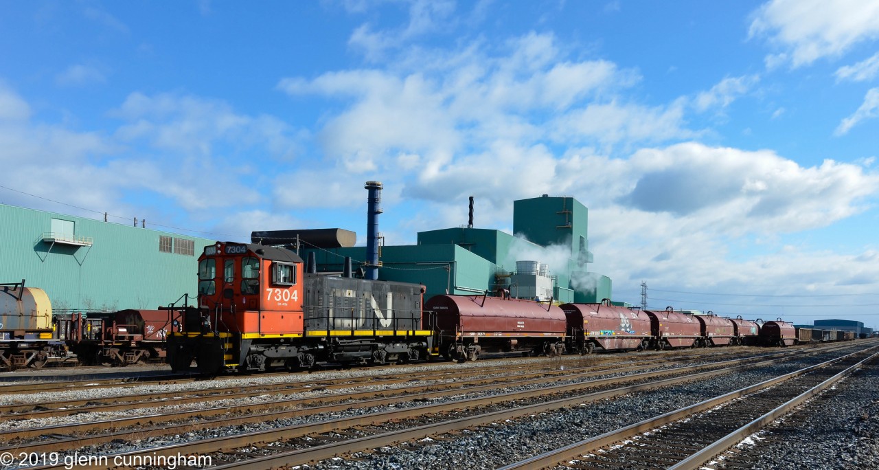 Retired CN SW1200 7304 is switching CN's Parkdale Steel Centre in Hamilton next to the Grimsby Sub. The sun and blue sky cooperated as the crew pushed this cut into the steel centre for processing.