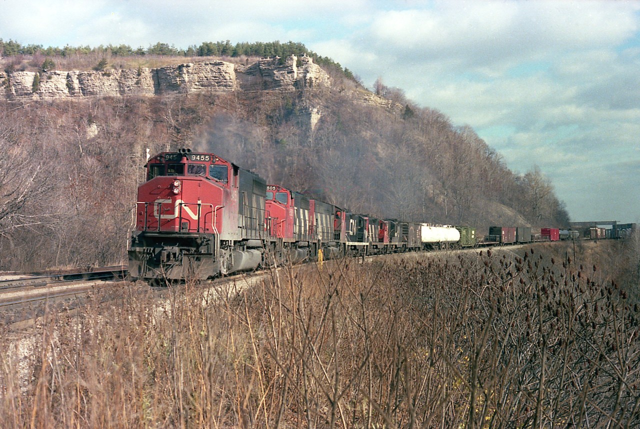 Here's a good healthy looking CN westbound on a rather nice mid-November day. Judging by how high the sumac is in this image, I would imagine the next year was the last for shooting this full curve.  It doesn't take long for sumac to grow, and it was impossible to hack some of this down because of the steep slope it is growing on. There were 90 cars of mixed freight on this train, with caboose #79337 on the rear. Power up front,three widecabs and three geeps. CN 9455, 9505, 9446, 4519, 4566 and 4565.
The Canada Crushed Stone overhang in the extreme background is still intact, despite the operation having been shut down around 5 years previous.