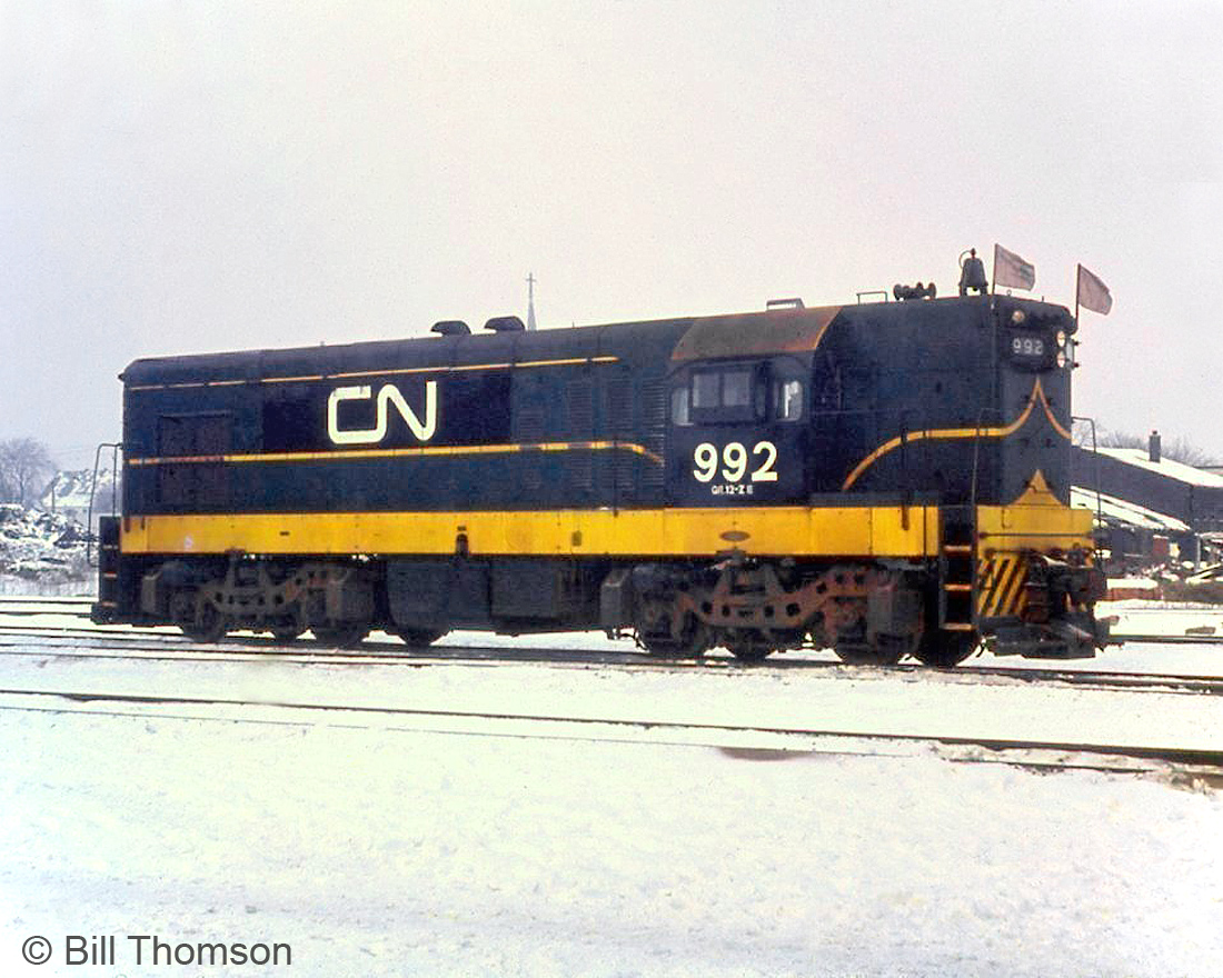 CN G12 992 is seen at London in 1966. This unit was originally purchased by the London & Port Stanley Railway from GMD London and delivered in July 1957 as L&PS L5, following an earlier unit purchased in September 1955 and numbered L4. The EMD/GMD G-series were export models, and smaller in size and clearance profile than a standard North American 4-axle locomotive at the time.When CN purchased L&PS in 1966, the two units were renumbered 991 & 992, eventually being repainted into CN colours. In 1969 both G12's were sent west and worked CN's Vancouver Island operations in BC for a number of years. Around early 1976 both were sent east to CN's Newfoundland operations and ended their lives serving as parts units for the fleet of narrow-gauge G8's on the island.