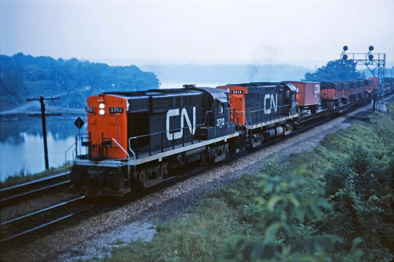 At dusk, CN RS18 3712 and C424 3214 lead piggyback train 252 through Bayview at the start of its trip to Montreal. Note the container flats with Dofasco steel several cars back.