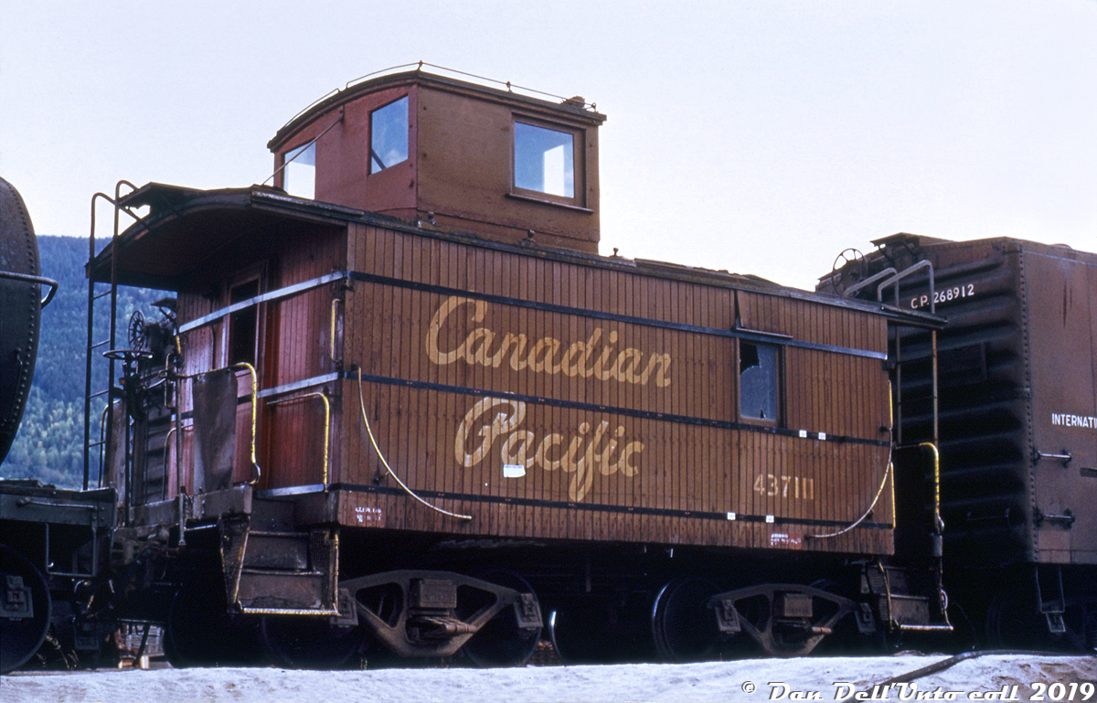 Having seen better days, decrepit CP "shorty" van (caboose) 437111 sits between freight cars in the yard at Nelson BC, living out its final days in service sporting broken and missing windows, damaged roof and tongue-and-groove wooden siding, and held together with bands of steel strapping wrapped around the entire length of the carbody.

From what I've been able to glean about this unique specimen, it was one of two steel underframe vans originally built in the 1930's as 34'10" long cars that CP cut down to 24'10" in 1944 for use on the Rossland Sub, in order to maximize the number of cars handled through one of the switchbacks along the line. The Rossland Sub was home of the Cominco smelter in Trail BC, located at the top of the steep 4.1% grade known as Warfield Hill. In the steam era, CP briefly employed a trio of Lima Shays to conquer the grades on the line in the early 1900's. In the early 70's, CP's last three Train Masters held down the assignment until they were moved to work the hump at Alyth Yard, their final job before retirement.

One account mentions when the Rossland Sub was cut back, the two shorty vans were used elsewhere - notably Nelson Yard for backup moves from Kootenay Forest Products at the east end of town. Apparently 437111 may have been involved in an incident with a yard engine at some point, and operated for a time in the sorry state shown here (apparently the banding was added sometime between August and October 1974) until being retired and scrapped.

Sister shorty car 437110 was in better condition and fared a bit better: it was eventually given the "plywood treatment", and made its way out east to serve in Montreal transfer service into the 1980's. Apparently efforts were made to save it when it was retired and sent from St. Luc to Weston for disposal, but things didn't pan out in the end for the ol '7110.

Two other known CP shorties were 435000 and 437134, but not much information can be found about them or their intended use.

Duplicate slide, photographer unknown (possibly Stan Styles), Dan Dell'Unto collection slide with some editing/cleanup.