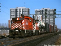 CP SW1200RS units 8123 and 8151 work the 2nd Oakville job, heading westbound through Obico on the Galt Sub in the late morning with a train of 10 cars and steel van 434010 in tow. The train is enroute for CN's Oakville Sub via the Canpa Sub, as CP long had trackage rights on CN between Toronto and Hamilton dating back to the TH&B days. Behind the power are seven brand new Ford "Louisville" L-series truck tractors (built in Louisville KY) riding saddleback style on their flatcar, and a cut of auto parts boxcars visible on the head end, likely bound for the Ford plant in Oakville. Being November, the lead SW1200RS has already been "winterized" with a painted plywood snow shield applied to its front handrails, designed to prevent snow build-up in the radiator shutter area.
<br><br>
<i>Peter Jobe photo, Dan Dell'Unto collection.</i>