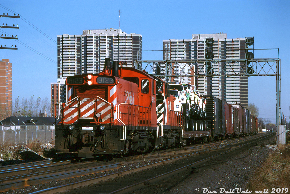 CP SW1200RS units 8123 and 8151 work the 2nd Oakville job, heading westbound through Obico on the Galt Sub in the late morning with a train of 10 cars and steel van 434010 in tow. The train is enroute for CN's Oakville Sub via the Canpa Sub, as CP long had trackage rights on CN between Toronto and Hamilton dating back to the TH&B days. Behind the power are seven brand new Ford "Louisville" L-series truck tractors (built in Louisville KY) riding saddleback style on their flatcar, and a cut of auto parts boxcars visible on the head end, likely bound for the Ford plant in Oakville. Being November, the lead SW1200RS has already been "winterized" with a painted plywood snow shield applied to its front handrails, designed to prevent snow build-up in the radiator shutter area.

Peter Jobe photo, Dan Dell'Unto collection.
