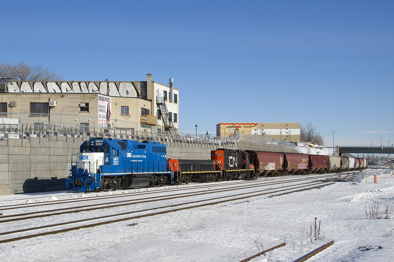 The Pointe St-Charles Switcher has left its namesake yard with empty grain cars destined for Taschereau Yard as it heads west on the transfer track of CN's Montreal Sub with leased GMTX 2257 leading and CN 227 and CN 7233 trailing. Up until the end of last summer the tracks curved off to the right here, but they now curve off to the left since a new right-of-way entered service then.