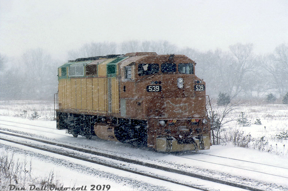 While this mystery unit is in unpainted primer, hints of green on the pre-painted components and the numberboards reveal her identity: brand new GO Transit F59PH 539, still in an unpainted and semi-primered state, stretches her legs on the test track at the GMD London locomotive assembly plant on a snowy winter's day. At the time GMD was building GO Transit's second order of F59PH commuter locomotives, units 536-547 (GCE-430h class) and 539, serial number A-4878, was the 4th unit constructed. She would hit the paint shop and emerge fully painted and lettered for her new owner a week or two later, along with sister unit 538.  The F59PH invasion would continue for a further two orders, and completely eradicate the remaining pre-F59 power from GO's roster (the GP40-2W's, F40PH's, rebuilt ex-ROCK GP40-3's and APCU/APU F-units). 539 would solder on for two decades in commuter service, until eventual retirement and sale Rosen Beaudin (RB) Leasing in March 2010 with a few sister units. While RBRX has sold off almost all of its ex-GO F59's (and scrapped a few), 539's disposition after is unknown.  Gord Taylor photo, Dan Dell'Unto collection slide.
