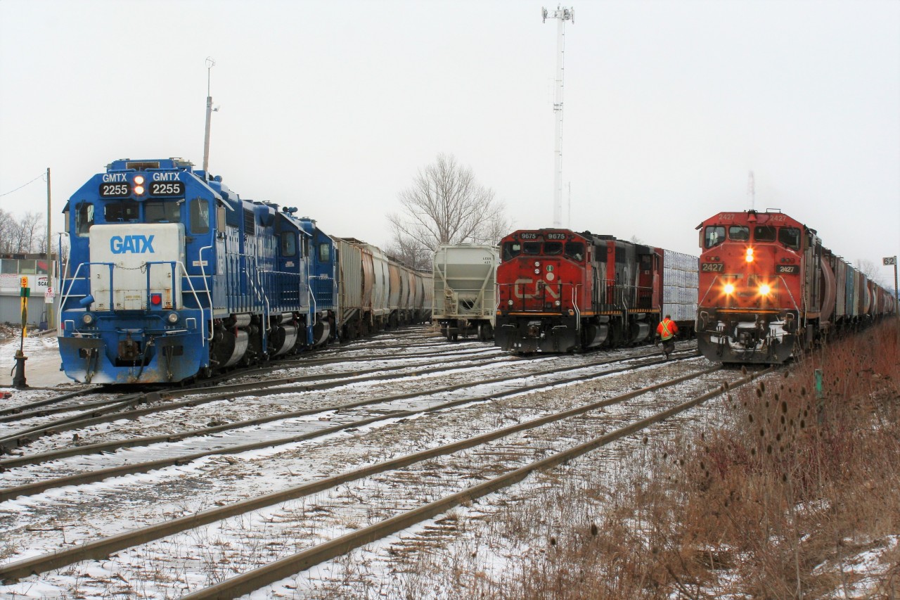 During the night of February 10, CN A431 with 9675 and 9482 had a long and heavy train when it departed MacMillan yard in Toronto. Once on the Guelph Subdivision, the Niagara Escarpment grade proved too powerful for the two four-axle units. The train retreated back to (Silver) Georgetown and set-off the majority of its Stratford cars before trying another run at the grade. Eventually the units made it over and then go on to set-off 39 cars in Guelph before finally arriving in Kitchener after sunrise. The train then tied-down in Kitchener and CN would order an X431 to lift the cars left on the Halton Subdivision by A431 and bring them the remaining distance to Kitchener. Here pictured in the Kitchener yard from left to right, CN train L568 with a trio of GMTX units waits on the yard lead across from A431’s power from the night before while X431 with 2427 has just arrived with a long train of hoppers.