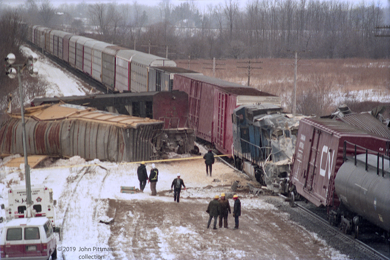 Excerpt from TSB Report - http://www.bst-tsb.gc.ca/eng/rapports-reports/rail/1995/r95s0021/r95s0021.asp 
On 16 February 1995, at 0349 eastern standard time (EST), a Canadian National (CN) freight train, travelling eastward on tangent main track at Mile 4.2 of the Strathroy Subdivision in London, Ontario, collided with the rear of a stationary freight train. The force of the collision propelled the stationary train eastward where it collided with another stationary freight train. Two employees sustained serious injuries. 
Looking west from Hyde Park Road overpass in the daylight of the morning of the crash (apparently)  we see the situation at the primary collision site prior to cleanup.  The autoracks of eastbound train 272 on the south track look OK,  but 2 of its front-end hi-cube boxcars derailed.  Three tail-end boxcars and a hopper from train 308 derailed, some are very mangled and the north track is blocked. 
In the collison, 272's lead engine CN 2105 (Bombardier HR616 cowl) derailed and was spun away from the tracks by the impact with train 308.  It was scrapped.
Trailing unit LMSX 723 (4 month old GE Dash 8-40CW) continuing forward by the inertia of its train, overtook CN 2105.  LMSX 723 derailed but remained in line with the tracks in its original direction, suffering various impacts.  It was sent to co-lessor Conrail's Altona PA shops, repaired and returned to service. 
For more detail, I recommend the TSB report above, very informative and reads well.