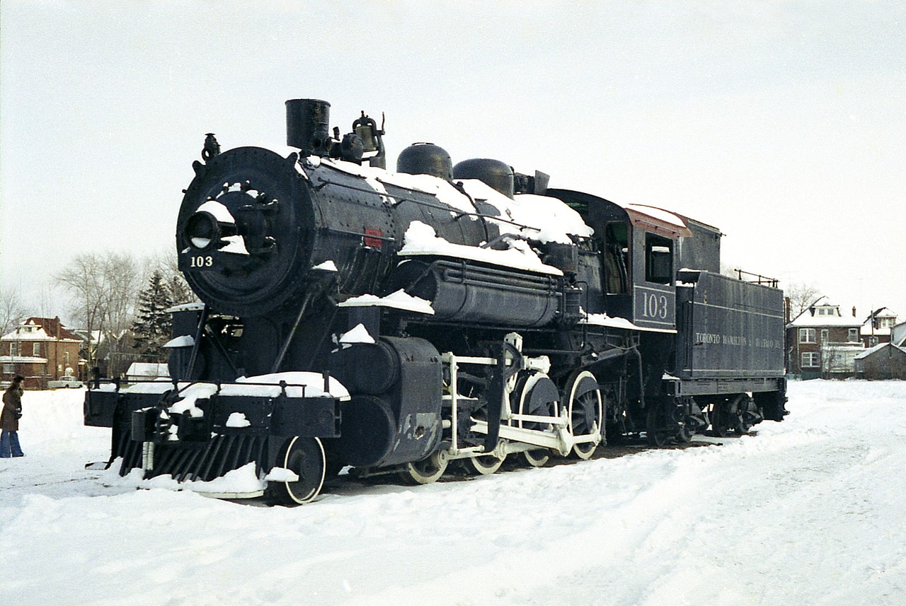 A photo such as this has my mind rocketing to the realization that I have made it to geezerdom. For TH&B 103 was a fixture in Gage Park by the Kinnear Yard for as long as I could remember in my youth, and I was rather shocked when doing a caption for this image that it was hauled out of that location over 40 years ago already. I had taken a few photos of it, but news that it was to be moved to Wentworth Pioneer Village meant the fence surrounding it was coming down, and it would be open for a nice shot. So, about two days before it was lifted by crane and trucked out I captured this image.
On the 18th of January 1977 it was hauled down Main St (the wrong way, no less!)  in Hamilton via flatbed truck to the Claremont Access to Upper James to Hwy 52 and onto 8 and to the new site near Rockton. There, it would be free from all the damage caused by Hamilton vandals.
Wentworth Pioneer Village closed in the mid 1980s citing financial troubles. Fortunately the place was reborn as Westfield Heritage Village, and some dedicated volunteers restored the old steamer, an undertaking that was completed in 2005.
There, she still sits. The Village is quite the attraction, and old TH&B 103 awaits your visit.