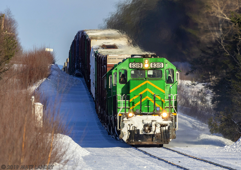 Shot at 600mm with my Sigma 150-600mm lens, a trio of green leads NBSR train 907, as they head down grade approaching Cork, New Brunswick. The telephoto shot makes the grade look steeper than it actually is.