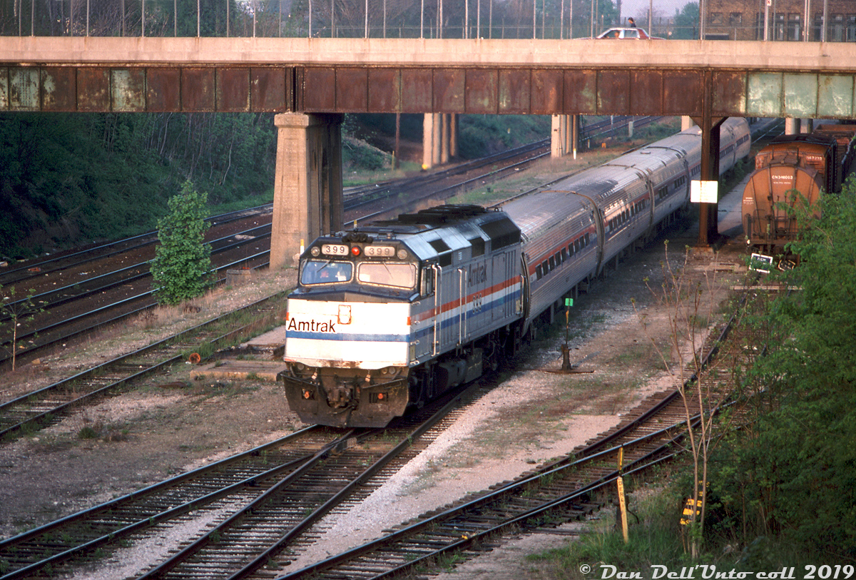Amtrak F40PH 399 heads up six Amfleet cars on the Toronto-bound "Maple Leaf" from the states, seen here in the evening light making its station stop at the former CN Hamilton (James Street) Station before continuing on to Toronto. By then the station and area in general was looking more than a bit run-down (I can't imagine it impressed the passengers from Buffalo much), with some station tracks in use by the CN car department for freight equipment repair (note the "blue flag protection" applied in front of the ore car on the right).This would be one of the final times the Maple Leaf stopped at the 1931-built James Street station: next week VIA (including Amtrak) would pull out of the station effective May 25th 1992 in favour of the new Aldershot station. GO Transit (who still ran Hamilton GO trains here) would move to the former TH&B Hamilton station in early 1993, leaving the station vacant. The Labourer’s International Union of North America (LIUNA) would eventually buy and renovate the station, and its now available for use as a banquet hall for special events. GO trains would return to this very area years later, but at the separate and newly-built West Harbour GO station.Bill McArthur photo, Dan Dell'Unto collection.