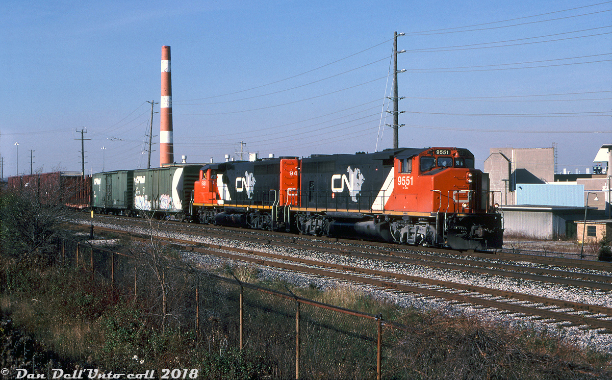 Operating on what was probably CN #577 or the equivalent, CN GP40-2LW's 9551 and 9461 (in matching CN North America paint) head south along the north service track of the Weston Sub through Malton with a string of cars to interchange to CP at West Toronto Yard. They're passing by just south of Malton GO station, passing the former Orenda Engines plant (now Magellan Aerospace) in the background. The tall concrete sections of the plant on the right were part of the engine test lab facilities where aircraft engines were put through their paces.The switch on the left off the south service track is for a spur that ran west through the middle of the International Centre parking lot and crossed Airport Road to access Boeing's Malton assembly plant (formerly McDonnell-Douglas Canada (MDCan), once the home of A.V.Roe where the Avro Arrows were built). In its later years the plant made wing assemblies and shipped them down to the Long Beach plant on special railroad wing cars. The operation lasted into the mid-2000's until Boeing closed and demolished the plant, and the spur was removed and/or paved over.John Eull photo, Dan Dell'Unto collection.