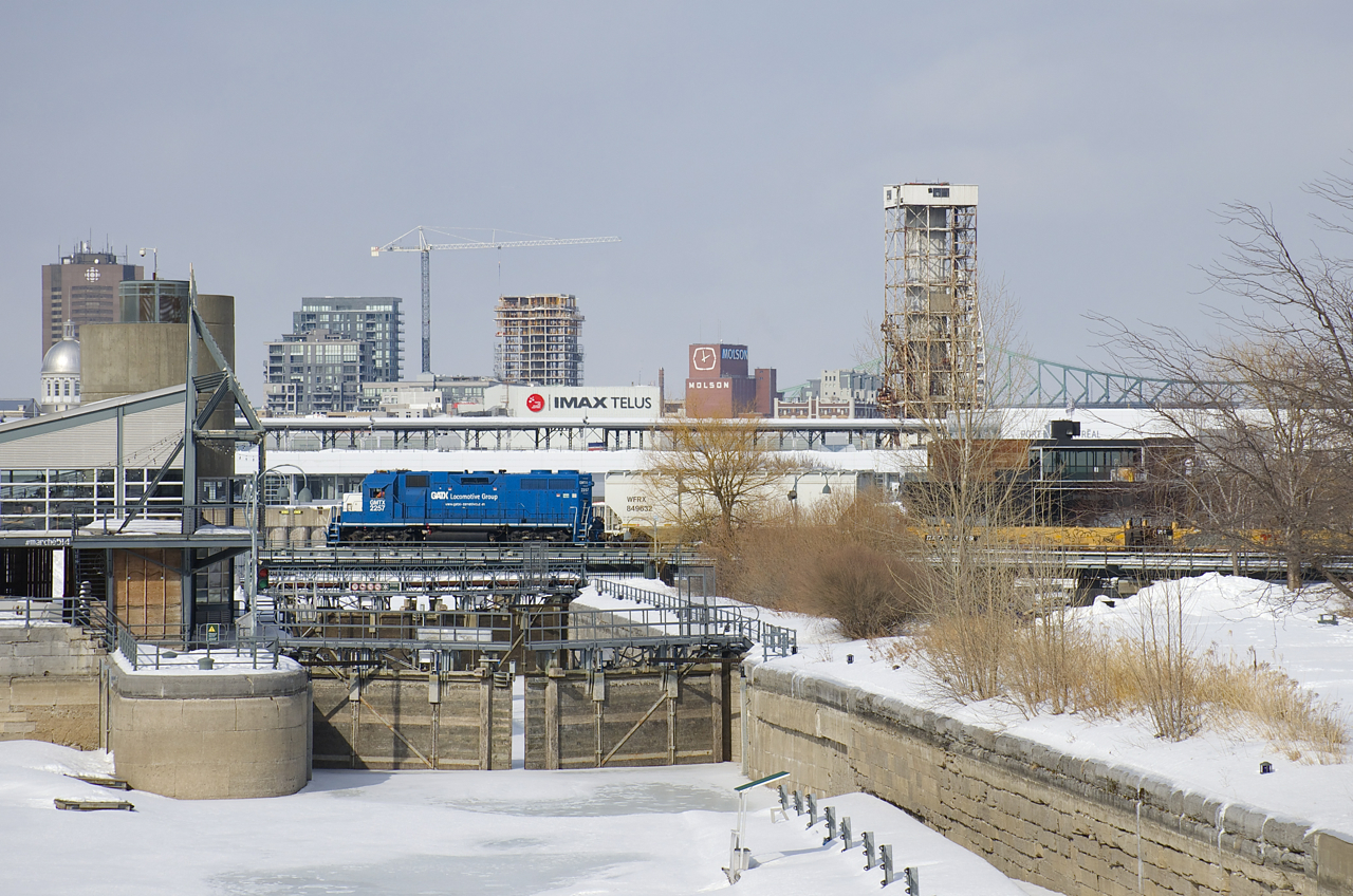 A transfer is entering the Port of Montreal as it passes the eastern end of the Lachine Canal, with GMTX 2257 leading a short cut of cars.