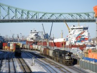 CN 596 is leaving the Port of Montreal with 61 empty grain cars and NS 9836 and NS 7592 running long hood forward on a sunny afternoon. At right the ships <i>CSL St-Laurent</i> and <i>CSL Laurentien</i> are laid up for the winter and above is the Jacques Cartier Bridge.