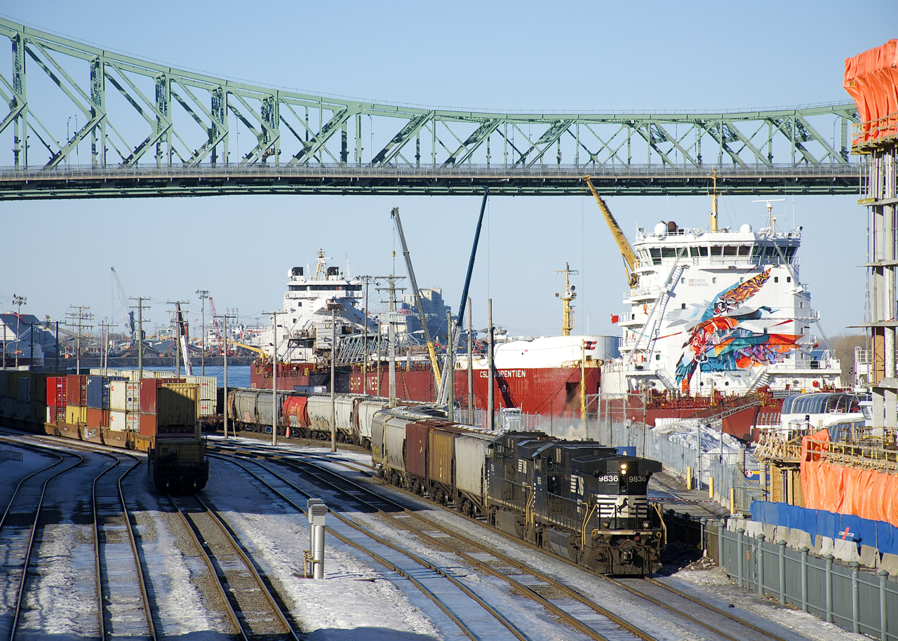 CN 596 is leaving the Port of Montreal with 61 empty grain cars and NS 9836 and NS 7592 running long hood forward on a sunny afternoon. At right the ships CSL St-Laurent and CSL Laurentien are laid up for the winter and above is the Jacques Cartier Bridge.