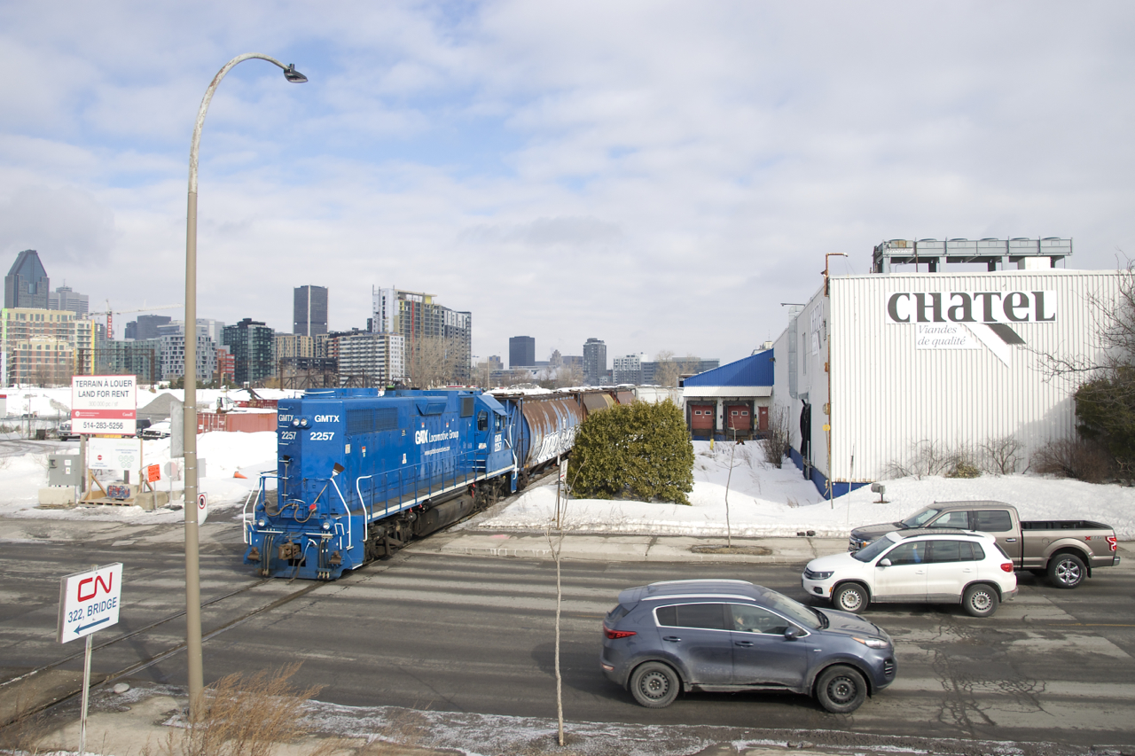GMTX 2257 is shoving ten grain cars towards the P&H mill as it crosses busy Bridge Street (which leads to the train/auto Victoria Bridge) on track PD10, which only sees rare movements towards this one customer.