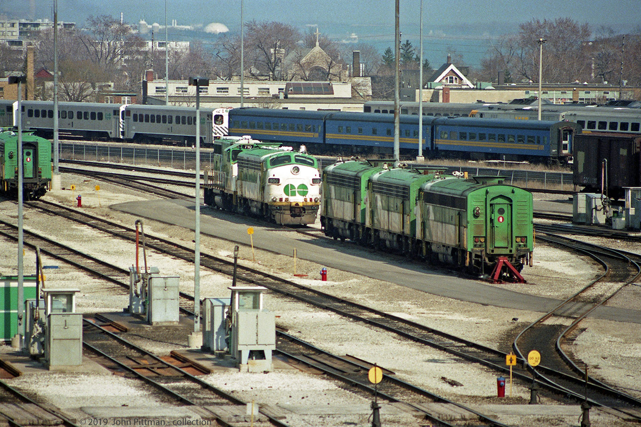 Islington Ave bridge over the yards of GO Transit's Willowbrook and VIA's Toronto Maintenance Centre (since 1985) has been a useful vantage point to see passenger equipment and locomotives since the overpass opened in Dec 1979.
Much has changed since this picture was taken. By the end of 1990, GO Transit had taken delivery of the majority of their F59PH locomotives, replacing APCU's, APU's, and older locomotives.  Similarly, VIA had completed its fleet of F40PH's. For several years after quite a lot of older equipment was stored in view of this bridge. 
Facing the bridge partly sealed up are APCU GOT 900 and GP40-2W GOT 710 - my Trackside Guide indicates most GO Transit GP40-2W's went to CN in 1991. Three other APCU's face the other way on that siding, plus another to the left.  Single-level GO Transit cab cars and blue VIA coaches can be seen on VIA yard tracks. The top of an LRC locomotive can be seen beyond the closest blue coach. 
All long gone, and I believe that GO Transit's fueling area was relocated a long time ago.