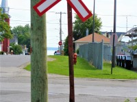 A railway crossing sign mounted on a homemade post guards Ingredion Canada's 1.5 mile industrial spur that connects its former Canada Starch Company (CASCO) facility to the CN Kingston Subdivision at mile 104.8. This was at the first crossing outside the large facility in the town. 