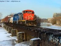 CN 542 with a rather large train passes over the Speed River in Hespeler. The Fergus subdivision, now a spur, was built by the Galt & Guelph that was taken over by the Great Western in 1860, and in 1882 absorbed by the Grand Trunk Railway. Still Later in 1923 CN.<br><br>  First built in 1857, the stone abutments likely dating to around this time maybe +20 years - but per Grand Trunk drawings of the bridge, the steel girder atop was likely installed in 1907 by the GTR. In 2018 not long after the takeover from GEXR CN completely re-decked the entire structure in a move unseen since the end of steam in 1959! The guard rails that survived to the end of GEXR dated to the 1870's.<br><br>  The town ever changing, of several mills built by the town founder, Jacob Hespeler, one is being converted into Condos in the far right background. <br><br>  That site, later known as an American Standard steel manufacturing  operation also had direct rail service via the former Grand River Railway's (CP) Hespeler Branch. <br><br>  The GRR/CP Hespeler branch crossed the CN at a diamond behind me and ran along the river to the right of this photo to the mill. In 1991 CN took over direct rail service to the plant when CP Abandoned a portion of the Hespeler branch due to the expansion of the 401. This eliminated the diamond and the Searchlight signals that protected it, but CN installed a switch to run down the embankment to the factory. <br><br>  Remnants of the rail line lingered into the early 2000's as crossbucks were still located at the American Standard site on Guelph St despite rails being pulled some years earlier.<br><br> I'll post some GEXR photos of this bridge later - it was quite scary to watch GEXR Trains cross this structure.<br><br>  Note: Some data (with additional notes from author added later) sourced from George Roth's book "Steel Wheels along the grand" - copies were once upon a time sold at Credit Valley Railway for those interested in this area. The maps and photos and history are very very much worth the price of admission. There's no way I could have known this without a good paper book - the Internet has nothing on that. Young kids - start collecting books on your favourite railway subjects. You won't regret it!