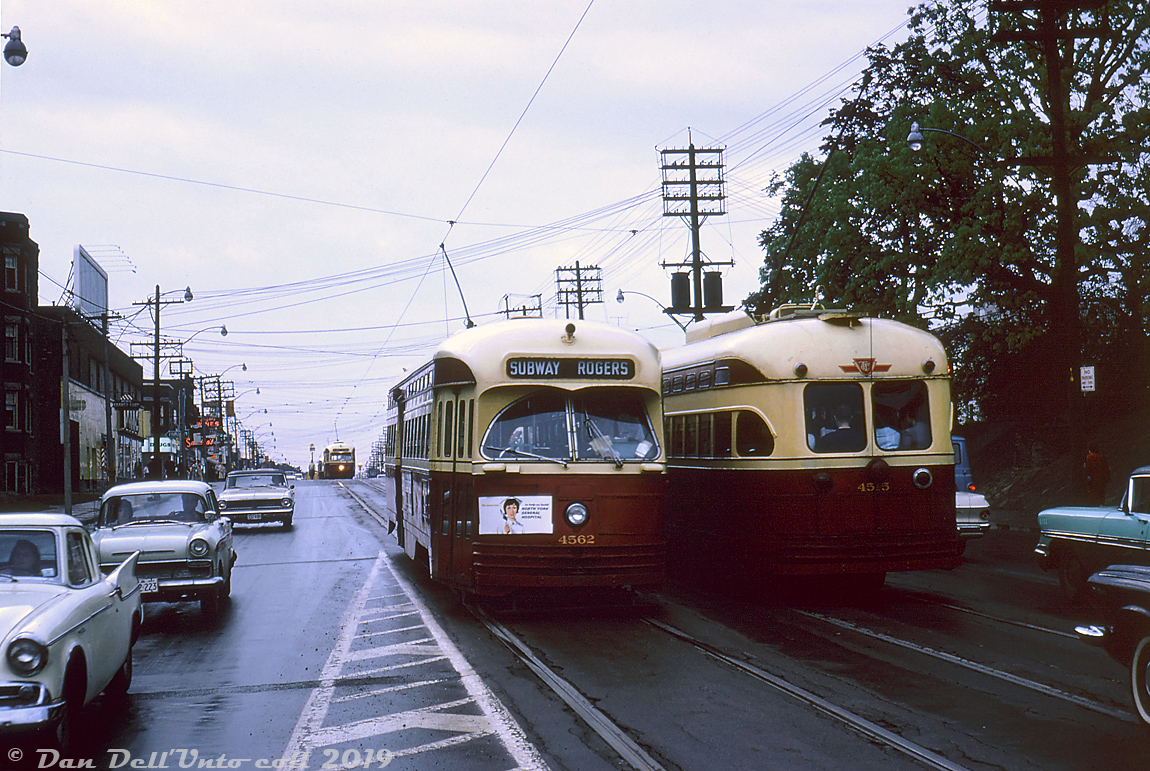 There's no shortage of streetcar action along St. Clair Avenue on this wet and gloomy Tuesday: TTC PCC 4562 (an A9-class car originally built for Cincinnati) operates on Rogers Road route, heading east to St. Clair Subway Station at Yonge Street after coming off Oakwood Avenue. It's passing packed A8-class car 4515 at Hilton Avenue, presumably operating on the St. Clair route westbound to Keele Loop. Judging by the traffic and two other PCC's are visible at the top of the hill at Bathurst Street, this is likely an evening rush hour shot.

Things are a bit different here today: where the streetcars are in the foreground would be part of the entry/exit ramps into the underground terminal of the St. Clair West Subway Station, built a decade later for the new Spadina subway line. Much of the surrounding buildings here have changed or been redeveloped as well.

For those curious, the ad on the front of 4562 reads "We need you...to help us build North York General Hospital", part of a public fundrasing campaign to help pay for construction of the new hospital that would get under way the next year and open to the public in 1968.

John F. Bromley photo, Dan Dell'Unto collection (with some editing and cleanup - this one was a little dark/underexposed).
