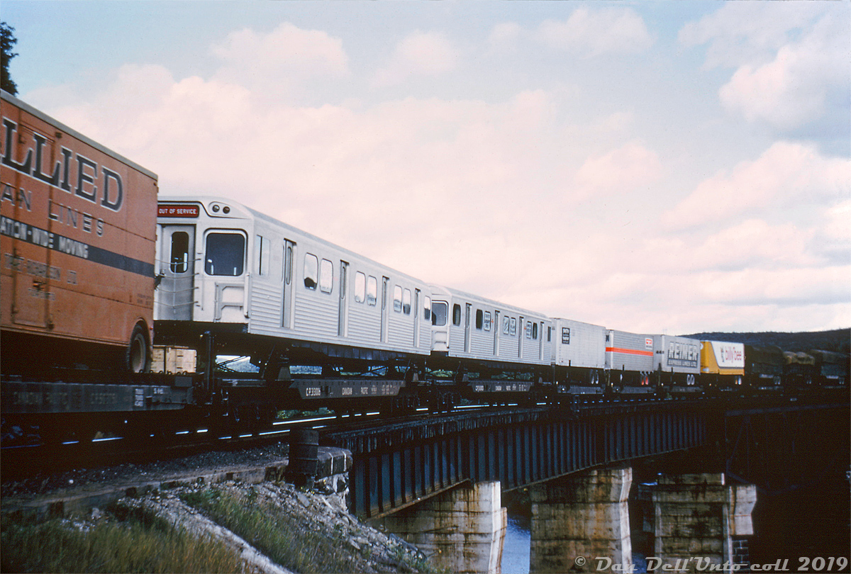 Those aren't piggyback trailers! Mixed in the consist of an eastbound Canadian Pacific Railway freight are a pair of brand new Toronto Transit Commission 5300-series H1 subway cars (riding on CP 313000-series flatcars built from cut-down heavyweight sleepers), making their way across the Little Pic River bridge at Mile 73 of CP's Heron Bay Sub. The two new cars, part of a 164 car order, are enroute from the Hawker Siddeley Canada plant in Fort William (Thunder Bay) Ontario where they were built. CP will handle them through northern Ontario and south to Toronto, where they will be interchanged to CN for final delivery to TTC's Greenwood subway yard off CN's Kingston Sub. 

Some nice "vintage" pig action is also visible: there are trailers for Allied Van Lines (moving company), Smith Transport (CP-owned), an unknown trailer with orange stripe, Reimer Express Lines (who kept the same logo for decades), Billy Bee (honey!), and some platform trailers with bullboard sides and tarpaulins, all riding on CP piggyback flatcars.

Duplicate slide - original photographer unknown, Dan Dell'Unto collection with some editing/cleanup (This slide was stamped for Robert McMann but no other information was noted on it (unusual for him), and northern Ontario was a bit out of his usual stomping grounds, so he likely acquired this duplicate in trade from someone at some point in time).