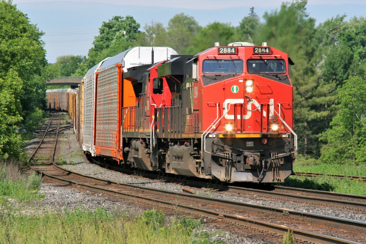 A long CN eastbound train with 2884 and 2036 rolls by the platform of the Georgetown station on an summer morning.