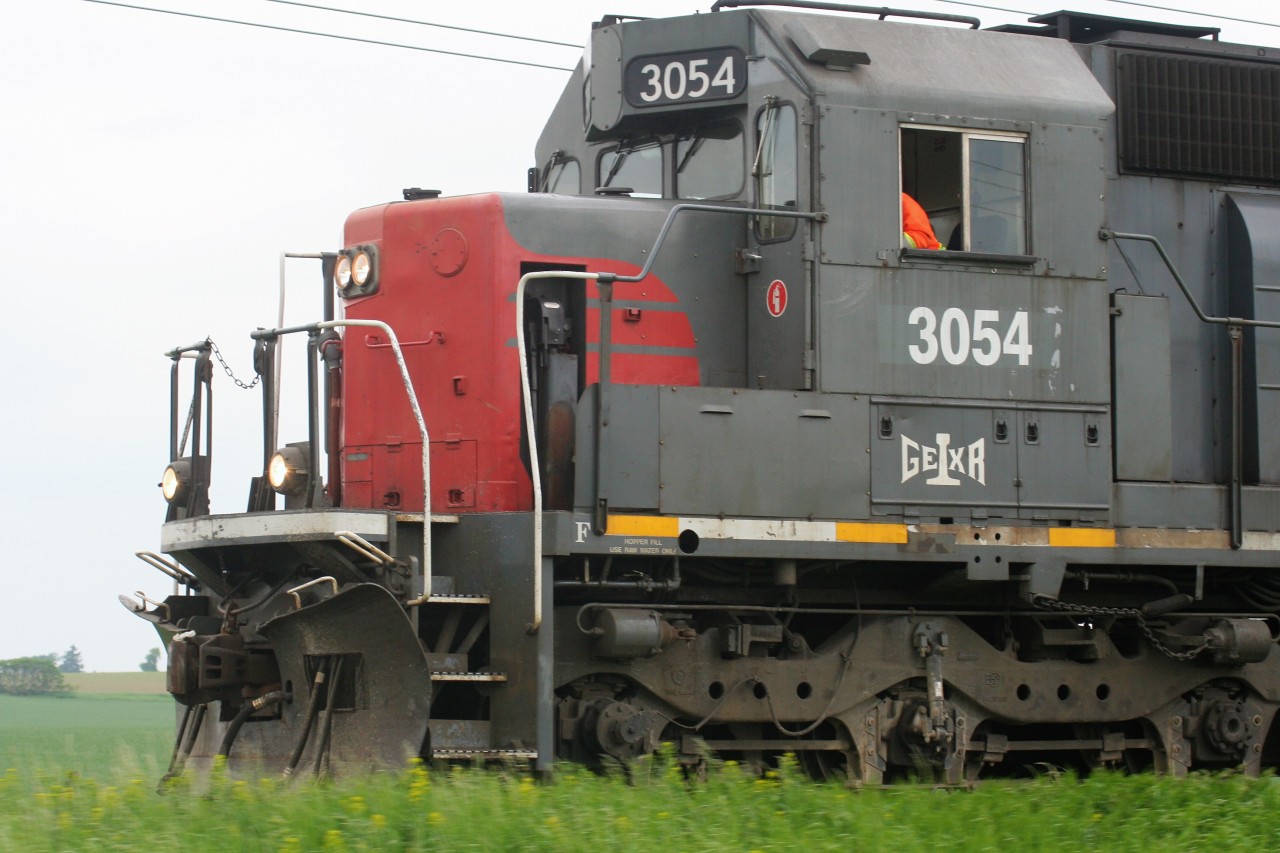 There are limited places in Southern Ontario where mainlines parallel busy roadways for several miles, however Highway 7 between Acton and Guelph is not one of them. The Guelph Subdivision runs beside the highway for many kilometers and has some interesting views. However, currently with only a limited amount of CN daylight freight movements in this section, GO and VIA Rail trains are now the main players. 

Photographed leaning out the window of a moving car, Goderich-Exeter Railway (GEXR) 3054 is seen overtaking traffic on Highway 7 as it leads 431 into Guelph on a warm summer afternoon.