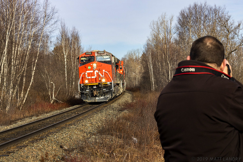 With another foamer perched nearby, a late Q120 rounds the bend at Berry Mills, approaching their next crew change point of Moncton, New Brunswick. This train hit a mudslide west of Edmundston, New Brunswick, (hence the condition of the units). Fortunately for everyone involved, the train stayed on the rails. 

April 14, 2019.