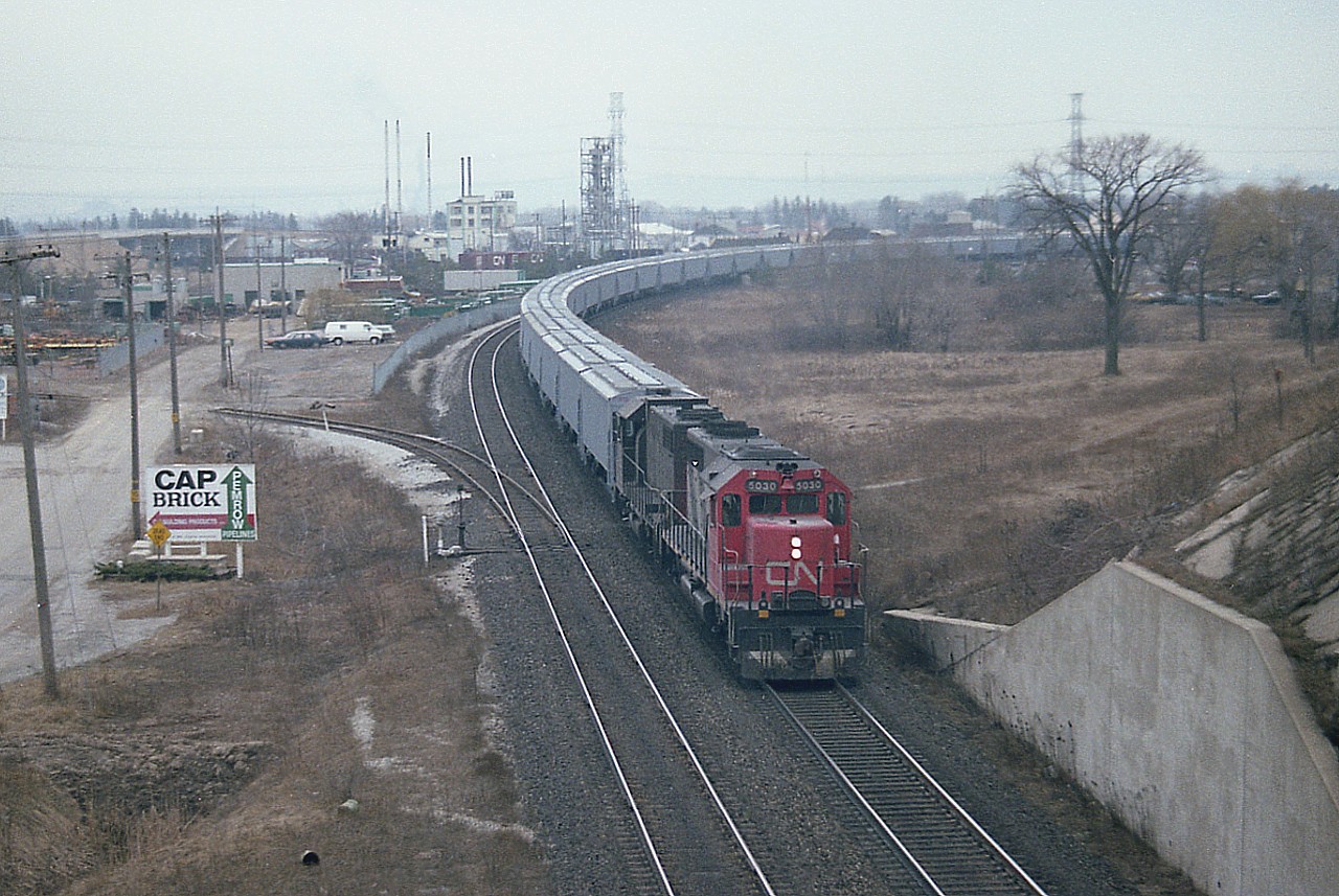 Here's an angle not often utilized. I'm standing on the old Hwy 2 bridge (later Plains Rd East) looking South. If the sun was out, this shot would not be possible. A unit train of some sort with a pair of SD-40s up front. In the background, left, one can see the Fariview Av bridge, and just to right centre behind the train is the Burlington West station, barely visible. And behind that, the chemical operations and the yard that once was a busy place. The train is just coming off the Oakville onto the Halton, Toronto-bound.