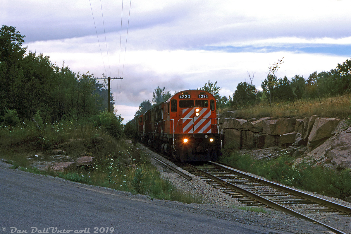 Passing through rock cuts south of Long Lake, CP 4223 leads two other MLW C424 sisters heading southbound on the Nephton Sub at County Road 44 crossing (Mile 10), heading back down to Havelock with traffic from Nephton and Blue Mountain. Timetables indicate the speed on this line in 1987 was a pokey 30mph max, with some 20mph stretches, so the units wouldn't have been moving too quickly through here (although there are grades on the line to tax the power, including a few 1.8% - 2% climbs).  CP's Nephton Sub was constructed in 1954 through rock cuts and swampland as a 16-mile line (later extended to 20 miles) north from Havelock to serve the American Nepheline Ltd's nepheline syenite mines at Nephton and Blue Mountain, still in operation today under Unimin. Those mines are the sole traffic generated on the Nephton Sub, and very likely the main reason it and the Havelock Sub haven't been abandoned by CP yet.  Peter Mumby photo, Dan Dell'Unto collection slide.