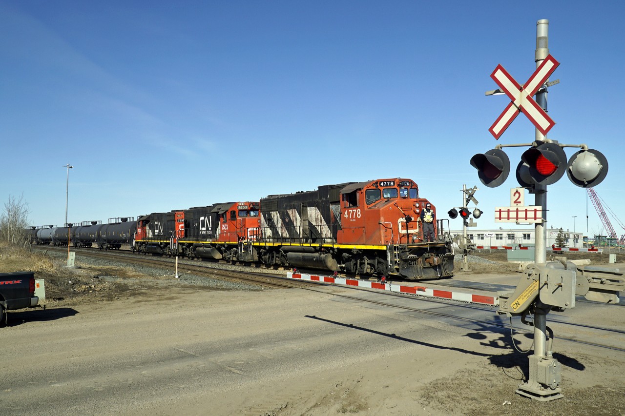GP38-2(W) CN 4778 and GP38-2 CN 7503 and 7530 are seen crossing Range Road 232 with a local move of oil tank cars.