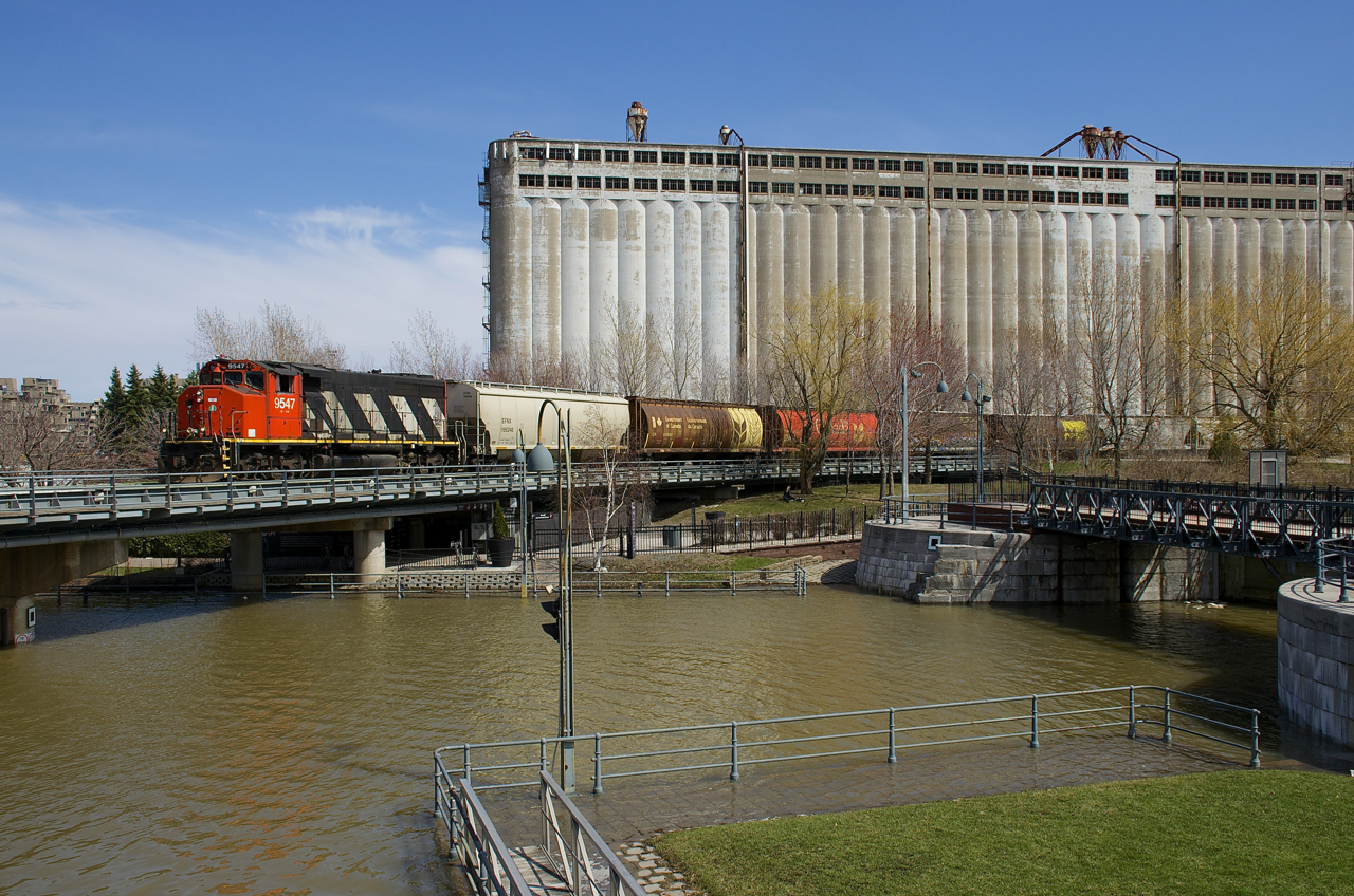 Water is very high in and around Montreal, with the army having been called in to help with flooding. The high water is evident as CN 9547 backs up towards the Bickerdike Pier, as it crosses the Lachine Canal with some grain cars.
