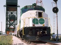 The Burlington Canal Lift Bridge looms high in the background over GO Transit GP40-2W 9810, seen stopped for photos on a fantrip special along CN's Beach Branch halfway between Burlington and Stoney Creek, at MP 4.9 "Hargrove" just south of the bridge.<br><br>This fantrip special (held during the US-based Electric Railroaders Association convention in Toronto) was run with three single-level Hawker Siddeley coaches, APCU 9861 at one end (rebuilt ex-Ontario Northland FP7 1512) and GP40-2W 9810 on the other. The APCU and GP40-2W were less than a year old at the time, having been acquired for the new Georgetown line service that began operations that April. This fantrip was part of a series of three* held on July 5th to 7th in the Toronto area, and from what I've been able to gather, photo stops included Stewarttown, Hamilton (James St.) station, Burlington Beach (here) and Burlington station.<br><br>The old Beach Branch, or more formally known as CN's Beach Subdivision, was originally constructed across Burlington Bay by the Hamilton & Northwestern Railway in 1876, running from Burlington to Stoney Creek. A notable feature along the line was this lift bridge, that let rail and road traffic cross Burlington Canal while also permitting ships entry into Burlington Bay and Hamilton Harbour. Queen Elizabeth Way freeway construction in 1974-75 severed the 7.8 mile line near the south end (still shown as a full line in the October 1974 CN ETT) and the line then operated as a 7.0 mile spur from Burlington for a few years until it was abandoned in 1981. CN ripped up most of the line in 1983, leaving short stubs at both ends to serve local rail customers. The single track across the lift bridge was removed and replaced by two more lanes of traffic during this period.<br><br><i>William J. Madden photo, Dan Dell'Unto collection slide.</><br><br>* Fantrips:<br>July 5th 1974: Toronto trolleybus fantrip with TTC Flyer E700's 9265 & 9312.<br>July 6th 1974: GO fantrip with GO GP40-2W 9810, three cars & APCU 9861 - with stops including Stewarttown, Hamilton Station, Burlington Beach, Burlington station.<br>July 7th 1974: TTC PCC fantrip with cars 4384, 4742 & 4750.