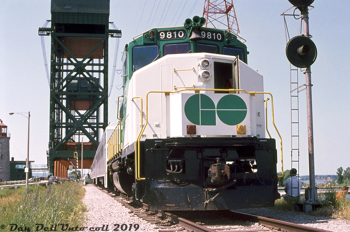 The Burlington Canal Lift Bridge looms high in the background over GO Transit GP40-2W 9810, seen stopped for photos on a fantrip special along CN's Beach Branch halfway between Burlington and Stoney Creek, at MP 4.9 "Hargrove" just south of the bridge.This fantrip special was run with three single-level Hawker Siddeley coaches, APCU 9861 at one end (rebuilt ex-Ontario Northland FP7 1512) and GP40-2W 9810 on the other. The APCU and GP40-2W were less than a year old at the time, having been acquired for the new Georgetown line service that began operations that April. This fantrip was part of a series of three* held on July 5th to 7th in the Toronto area, and from what I've been able to gather, photo stops included Stewarttown, Hamilton (James St.) station, Burlington Beach (here) and Burlington station.The old Beach Branch, or more formally known as CN's Beach Subdivision, was originally constructed across Burlington Bay by the Hamilton & Northwestern Railway in 1876, running from Burlington to Stoney Creek. A notable feature along the line was this lift bridge, that let rail and road traffic cross Burlington Canal while also permitting ships entry into Burlington Bay and Hamilton Harbour. Queen Elizabeth Way freeway construction in 1974-75 severed the 7.8 mile line near the south end (still shown as a full line in the October 1974 CN ETT) and the line then operated as a 7.0 mile spur from Burlington for a few years until it was abandoned in 1981. CN ripped up most of the line in 1983, leaving short stubs at both ends to serve local rail customers. The single track across the lift bridge was removed and replaced by two more lanes of traffic during this period.William J. Madden photo, Dan Dell'Unto collection slide.* Fantrips:July 5th 1974: Toronto trolleybus fantrip with TTC Flyer E700's 9265 & 9312.July 6th 1974: GO fantrip with GO GP40-2W 9810, three cars & APCU 9861 - with stops including Stewarttown, Hamilton Station, Burlington Beach, Burlington station.July 7th 1974: TTC PCC fantrip with cars 4384, 4742 & 4750.