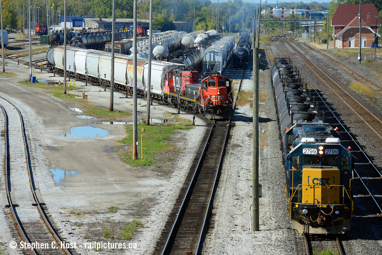 With the Sarnia station at top right, CSX's daily transfer is inbound to Sarnia withh a 12 car train while a CN yard job (Plank rd job?) switches the east end of "C" yard. Top left is the CN Roundhouse and "Bunkhouse" area, which a closer photo from 30 years earlier was posted by Mr. Pittman a few days ago. My photo was taken from Indian Rd overpass and gives a great overview of the area with lots of details - a train is also lined west on T2 through the tunnnel. Also notice in far top left the blue/white building? What was it used for? It has tracks leading right up to it... almost looks like an engine or car shop... not quite sure what it was used for now as I don't believe anything goes inside it today.