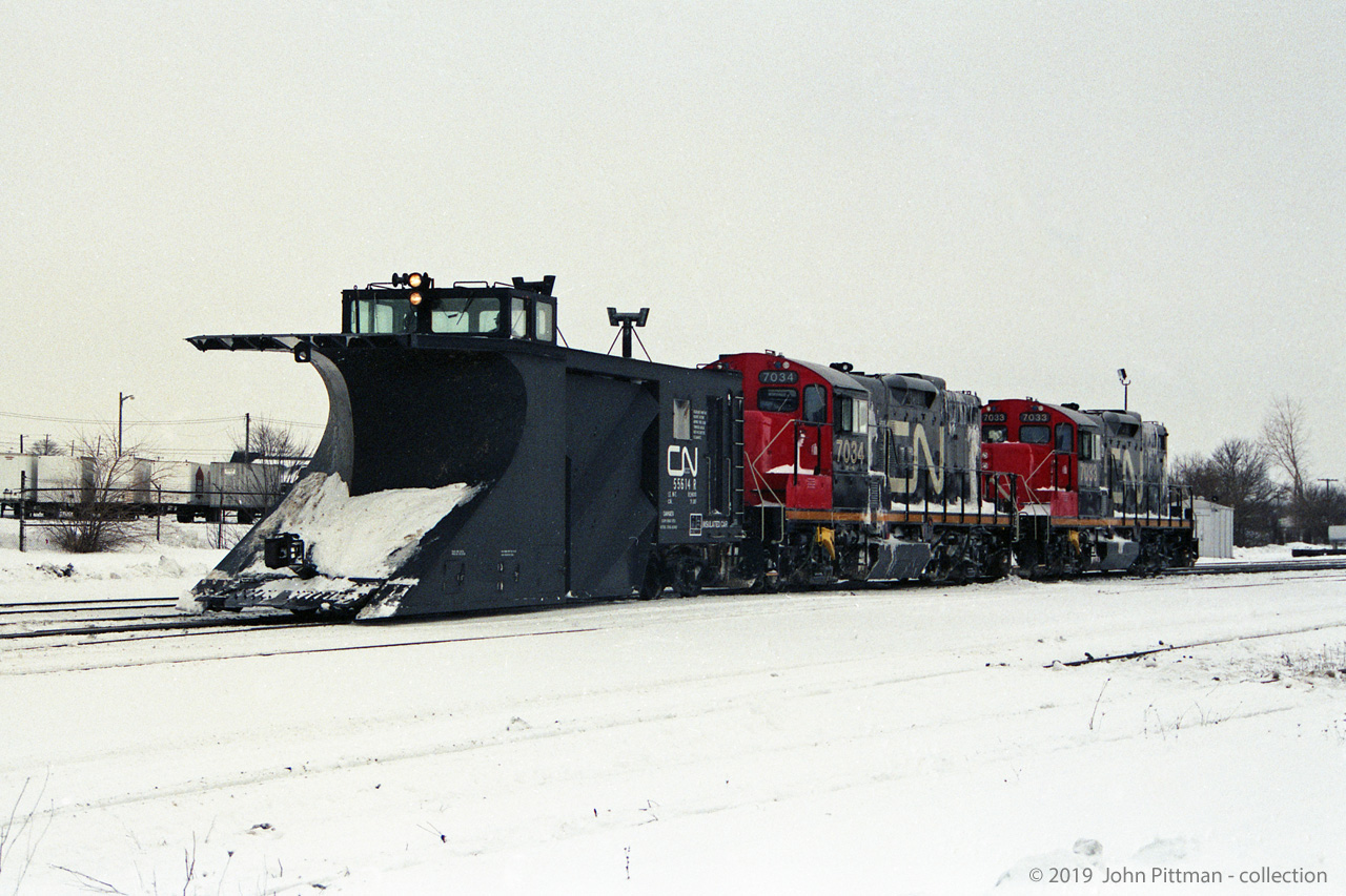 A CN plow train powered by GP9rm units CN 7034 and CN 7033 in the vicinity of CN London Yard. 
In other pictures the train was near Rectory Street grade crossing, with more snow on the plow.
Date is correct, location mapped is approximate.