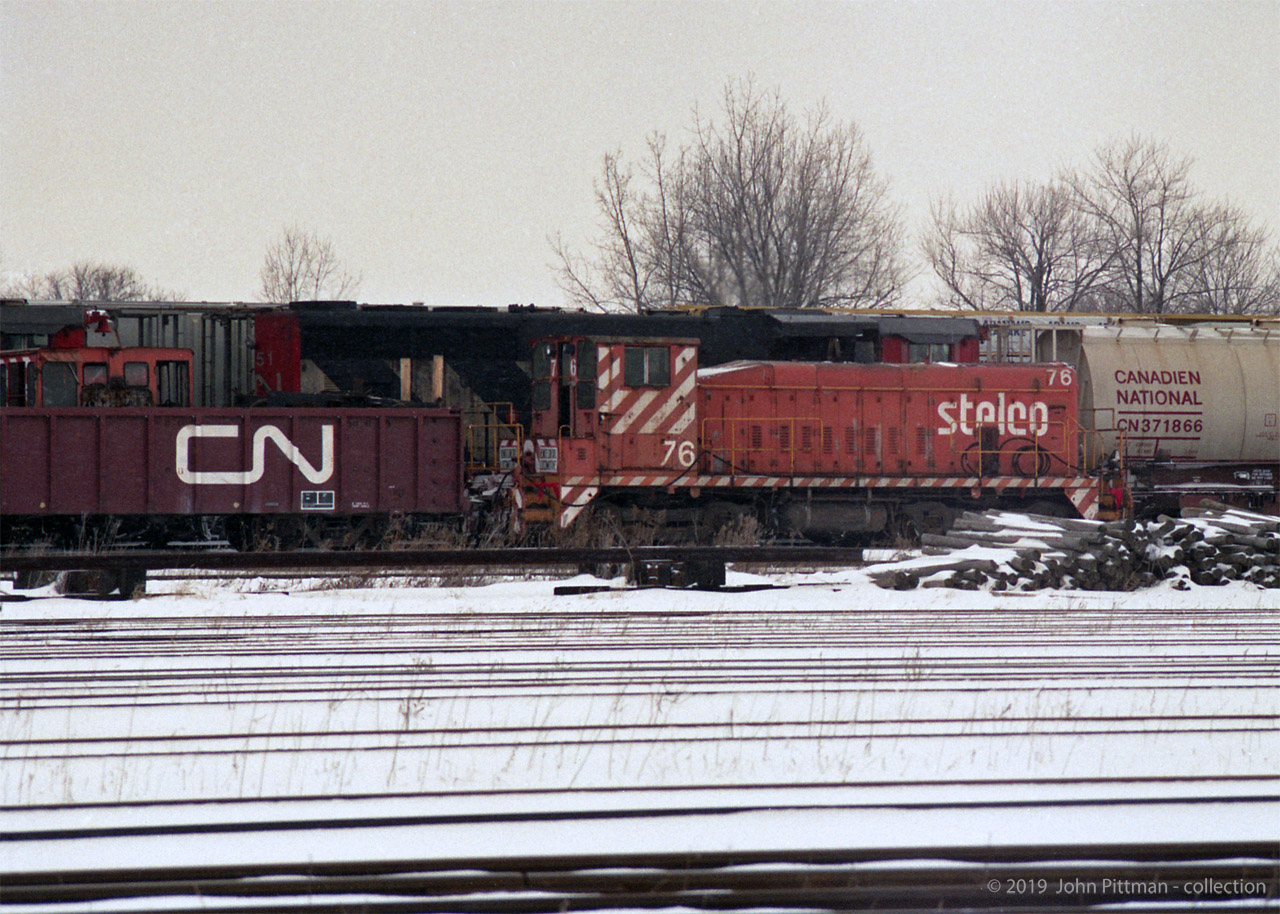 "There were 6 Stelco engines disposed of during Jan/Feb 1995. They all shipped CN to Windsor and then CSX to McDonald Ohio for buyer Larry’s Truck Electric.
SW-8 71, 74, and 76; SW900 78, 79; and G.E. 80ton 54.
The G.E. plus 74 and 79 were all in pieces, in gondolas, the others were able to move on their wheels." 
Quote above from Mr. Mercer's comment on my previous Stelco submission. 
In this image, the front of the cab of scrapped GE 80ton Stelco 54 is visible above the gondola side.  The red bell that appears to be above it is part of the CN locomotive on the next track.  
GMD SW8 Stelco 76 carries an air-brake jumper hose connecting the railcars on either end of it.
Location mapped is approximate.