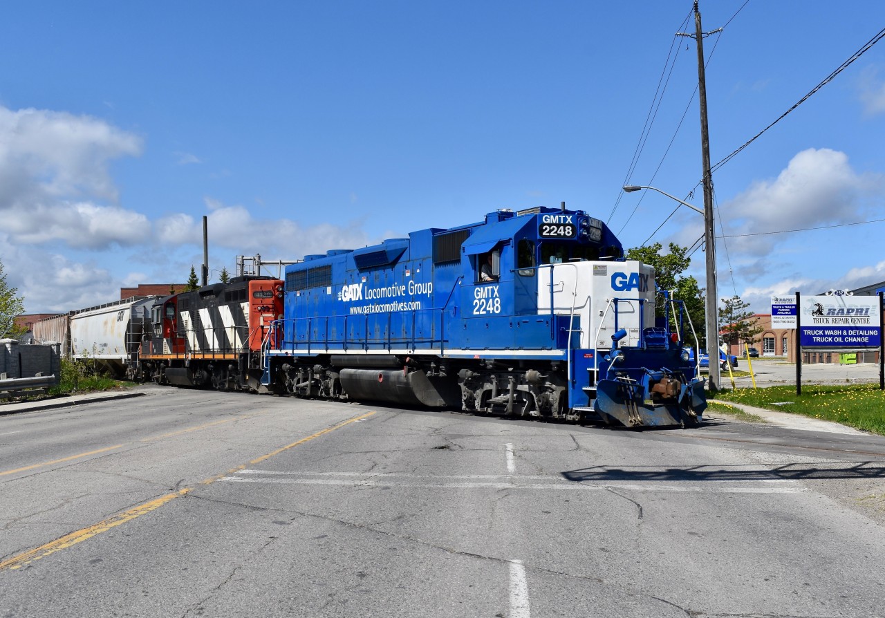 Backing down the Peel Village Industrial Lead with no more than 10 cars in tow, the power of today’s 559 is seen backing clear the busy 5 lane Clarence st crossing as they head down the spur southbound to service a few industries near Peel Village on Victoria Day Monday. Time was 10:41 and the power is GMTX 2248 and CN 4130
