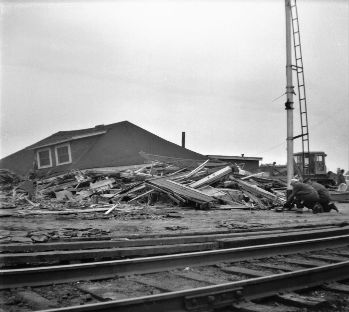 On the morning of Tuesday, August 31st, 1965, after westbound freight 401 passed, crews went to work to erase the old wood frame CN Pembroke Ontario station from the planet.  As the entire structure was deemed as scrap, no effort was made to save anything.  The process took only about an hour. In this shot, two workers begin t0 remove the old train order signal that stood in front of the old station. Location is approximate.