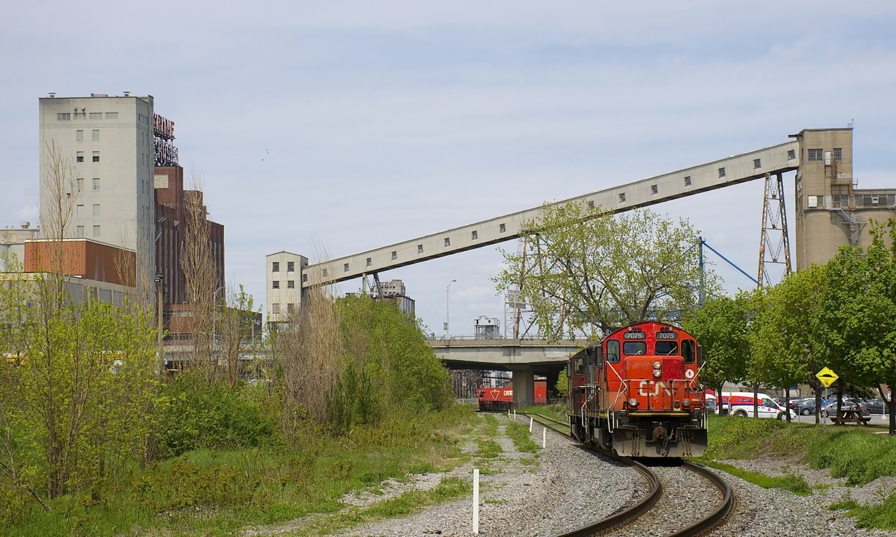 Grain infrastructure is visible in the background as GP9's CN 7075 & CN 7229 head east to pick up empty grain cars on track PC-27.