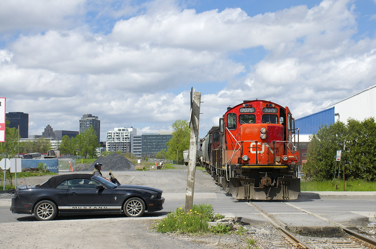 A Mustang waits for GP9's CN 7075 & CN 7229 to clear Bridge Street as they shove three loaded grain cars towards the P&H mill.