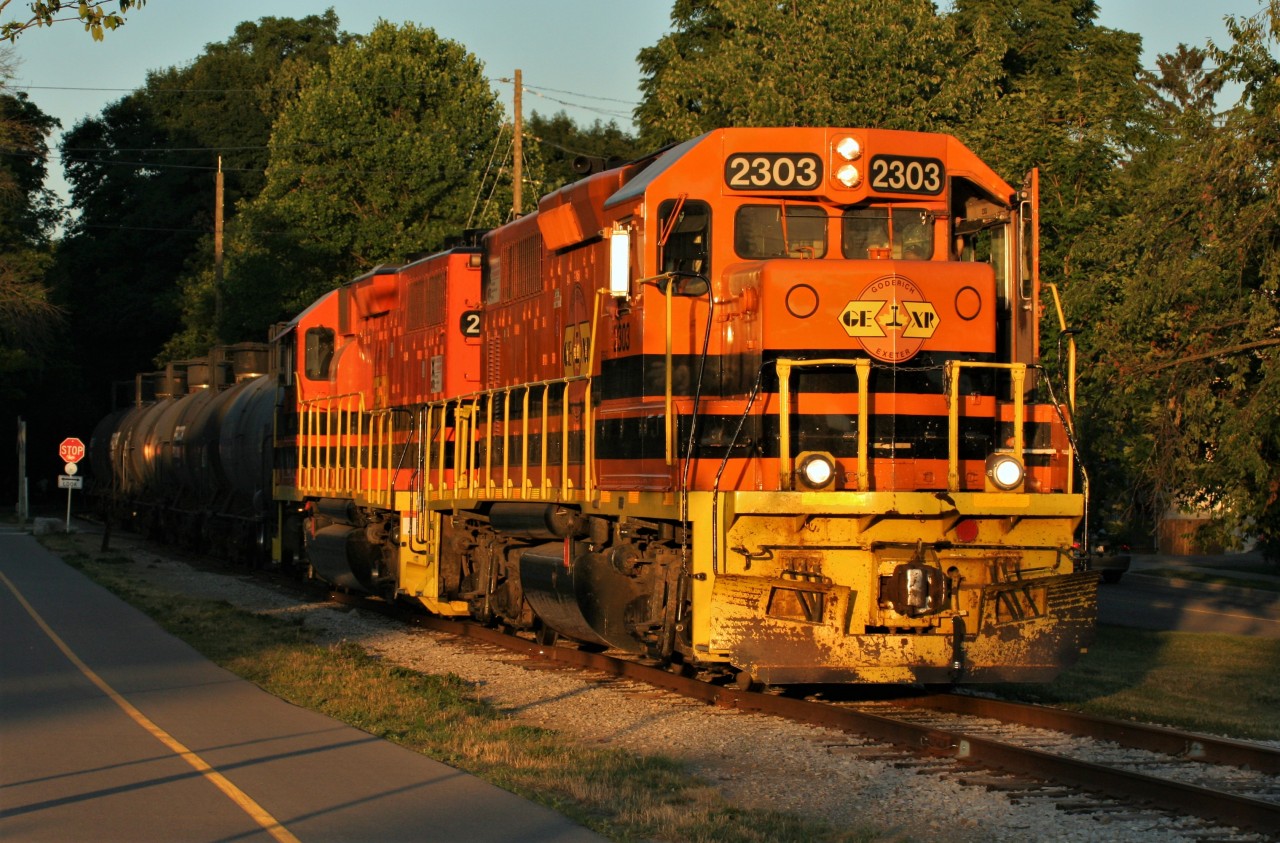 Emerging from the trees and shadows, Goderich-Exeter Railway (GEXR) train 584, is illuminated by the very last light of a fading summer day as it crosses William Street in Waterloo heading for Elmira on the Waterloo Spur. Powering the train are GEXR 2303 and GEXR 2073.