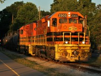 Emerging from the trees and shadows, Goderich-Exeter Railway (GEXR) train 584, is illuminated by the very last light of a fading summer day as it crosses William Street in Waterloo heading for Elmira on the Waterloo Spur. Powering the train are GEXR 2303 and GEXR 2073. 