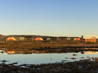 Shortly after the sun rises over the hillside, eastbound stack train Q120 comes rumbling by, giving off reflections at Upper Dorchester, New Brunswick. 