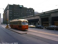 <b><i>"Toto, I have a feeling we're not in Kansas anymore"</i></b>: TTC A14-class PCC 4779, operating on a farewell fantrip for the TTC's fleet of secondhand Kansas City streetcars, is pictured facing west on College Street at Bay Street beside the iconic Eaton's College Street store. The 65 Dodson route exposure isn't one of the TTC's, rather, it is from a Kansas City rollsign installed in 4779 specially for the occasion. The usual selection of 70's automotive iron pictured lined up outside Eatons wouldn't be complete without an AMC Gremlin and VW Bug thrown into the mix.<br><br>The 30 TTC A14-class PCC streetcars (4750-4779, built 1946-47) were purchased secondhand from Kansas City in 1957 and were the last group of secondhand PCC's acquired by the TTC, but due to their condition they were the first ones to be retired and sold off. Most were resold to MUNI (San Franciso) and SEPTA (Philadelphia) for continued use, with the last one (4779) retiring a few months after this photo was taken. The TTC would continue to operate much of its other secondhand and purchased-new PCC cars in regular service until the last ones were retired in the 90's.<br><br>Opened in 1930, the Eaton's College Street store was originally envisioned to be a much grander complex (including a headquarters office tower) until the Great Depression caused Eatons to scale it down. The seven-floor Art-Deco department store building housed 600,000 square feet of retail space dedicated to house furnishings, furniture, fabrics and wall hangings, electrical appliances, China and linens, and included fashion and apparel specialty shops, a beauty salon, a portrait studio, a fine art gallery room, and an Art Moderne-styled 7th floor featuring a special restaurant and auditorium (to give an idea of how scaled-down it was, the original plans called for 5 million square feet of retail space!). The TTC for a time ran special inter-store Eatons shuttle buses between their flagship Queen Street and College Street stores. <br><br>But at the time of this photo Eaton's was well on its way to completing the first phase of its massive Eaton Centre development, including a new flagship department store with one million square feet of retail space off Dundas that opened a few months later in February 1977 and replaced both their Queen and College locations. Happily, the College Street store was spared the wrecking ball when it was sold off and turned into commercial retail and office space. Much of the heritage elements of the building have been preserved, including the restored 7th floor restaurant and auditorium used as a special events venue.<br><br><i>J. Bryce Lee photo, Dan Dell'Unto collection.</i>