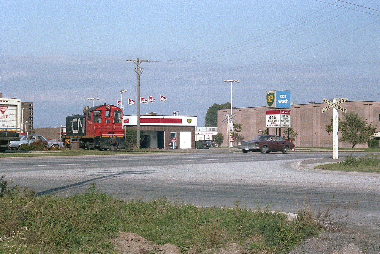 Just another little localized image for the fans who live in Niagara.....this is CN 7165 which this day worked the Port Weller line thru NorthEnd St. Catharines. The loco is stopped just short of Welland Av and I am across the street at the corner of Welland & Neilson. The lads have 'abandoned ship' for a run into Wendys (just out of sight on the left) for a snack.
The gas station, for those interested, originally was a Supertest station; all kinds of trouble putting the tanks in and anchoring them because in the 1970s this whole area was a thick swamp. The tanks wouldn't stay down. (gas is lighter than water) Supertest was taken over by BP around 1973 and now we see it is part of PetroCanada. Gas is 44.5 a litre, reads the sign, and the guy driving that heap about to cross the tracks should use some of the money he saves on gas to get himself a headlight.:o)
The SW8 switcher, built back in 1951, was retired by the end of the 1980s.