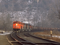 <b>DUNDAS. </b>A quartet of GP-40-2s handle a string of ore cars up the hill through the subdivisions namesake city of Dundas. Per information attained from   facebook via <a href="http://www.railpictures.ca/author/cv_acr?bwbps_page_7445=5">Chris van der Heide</a>, the suspect ore train is likely a slag train   origination loads is Subdury and hauling them to Paris (Thanks for the info by the way Chris). As further evidence, <a   href="http://www.railpictures.ca/upload/a-rather-noteworthy-lashup-on-an-eastbound-slag-extra-which-is-about-to-enter-the-oakville-sub-off-the-dundas-at-  bayview-junction-hamilton-rare-combination-even-for-back-in-the-80s-cn-2104-919">Arnold Mooney caught the same movement</a>, likely around the same time in   1984. Ore trains are not an unfamiliar site in southern Ontario. For many years, including the majority of the 80s at least (I'm unsure about the specific   timeline but curious if anyone else knows?), there was a regular ore train from Temagami on the ONR down to the blast furnace at Dofasco in Hamilton. This   bygone gem is well documented with <a href="http://www.railpictures.ca/main-page/back-in-the-days-of-the-ore-train-a-run-from-mines-in-temagami-to-hamilton-  for-dofasco-it-usually-got-5-units-gp40-2-or-sd40s-and-90-cars">Dave Brook's</a> and <a href="http://www.railpictures.ca/?attachment_id=23934">Glenn Courtney's</a> photos. On a side note, Dave, you said under Arnold's shot above that you worked a few of these trains, can't   help but wonder if you were on this one!?<br><br>Dundas was a popular place for railfans, drawing out many, as evidence by the railfans in this photo alone.   The aging scene is well documented throughout this era. <a href="http://www.railpictures.ca/upload/a-view-with-a-bit-of-everything-historical-the-old-  dundas-station-on-borrowed-time-as-steps-to-move-it-and-preserve-it-fell-thru-awaits-its-demise-as-via-75-with-a-rare-mlw-fpa-2u-6758-lead">The station</a>   likely drew many out, as it provided an accessibly yet secluded place to watch westbounds charge the grade. <a href="http://www.railpictures.ca/upload/cn-  5047-5525-westbound-pass-the-old-canada-crushed-stone-ltd-facility-near-mile-4-dundas-sub-this-image-while-a-tad-grainy-shows-a-rather-open-view-of-the-old-  rail-siding-which-led-up-to-the-larg"> Canada Crushed Stone</a> also provided a unique backdrop (<a href="http://www.railpictures.ca/?attachment_id=7210">and shooting platform!</a>). Norm especially seems to have had Dundas as a favorite location for a while (which makes me wonder   if you may have run into him here Arnold?). Fortunately, despite the fading access and encroaching trees, this location still draws in railfans in resent   years including <a href="http://www.railpictures.ca/upload/cn-train-no-435-sweeps-through-the-curves-at-dundas-ontario-with-an-assortment-of-power-that-has-  become-increasingly-common-as-of-late">Ryan Gaynor's</a> and <a href="http://www.railpictures.ca/upload/cn-148-glides-down-dundas-peak-is-this-elevated-  enough-or-what">Jude B's</a> recent shots. 