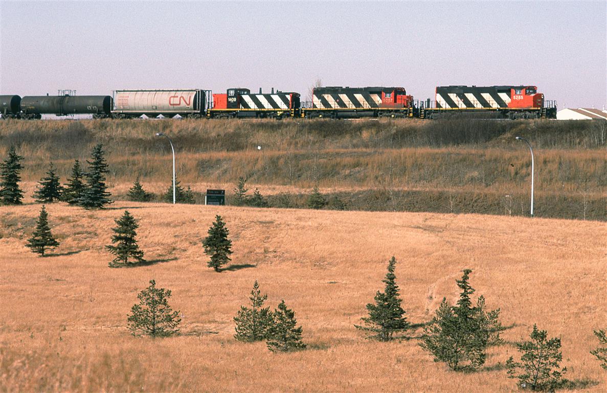 424 is on the embankment approaching the big bridge over the North Saskatchewan River. In tow, is a GMD-1 that I am assuming was destined for Wainwright yard.
Westbound Highway 16 is hidden by the fill in the foreground, while the eastbound lanes are out of frame at the bottom. Just a sign and a couple streetlights give clues to the existence of the road.