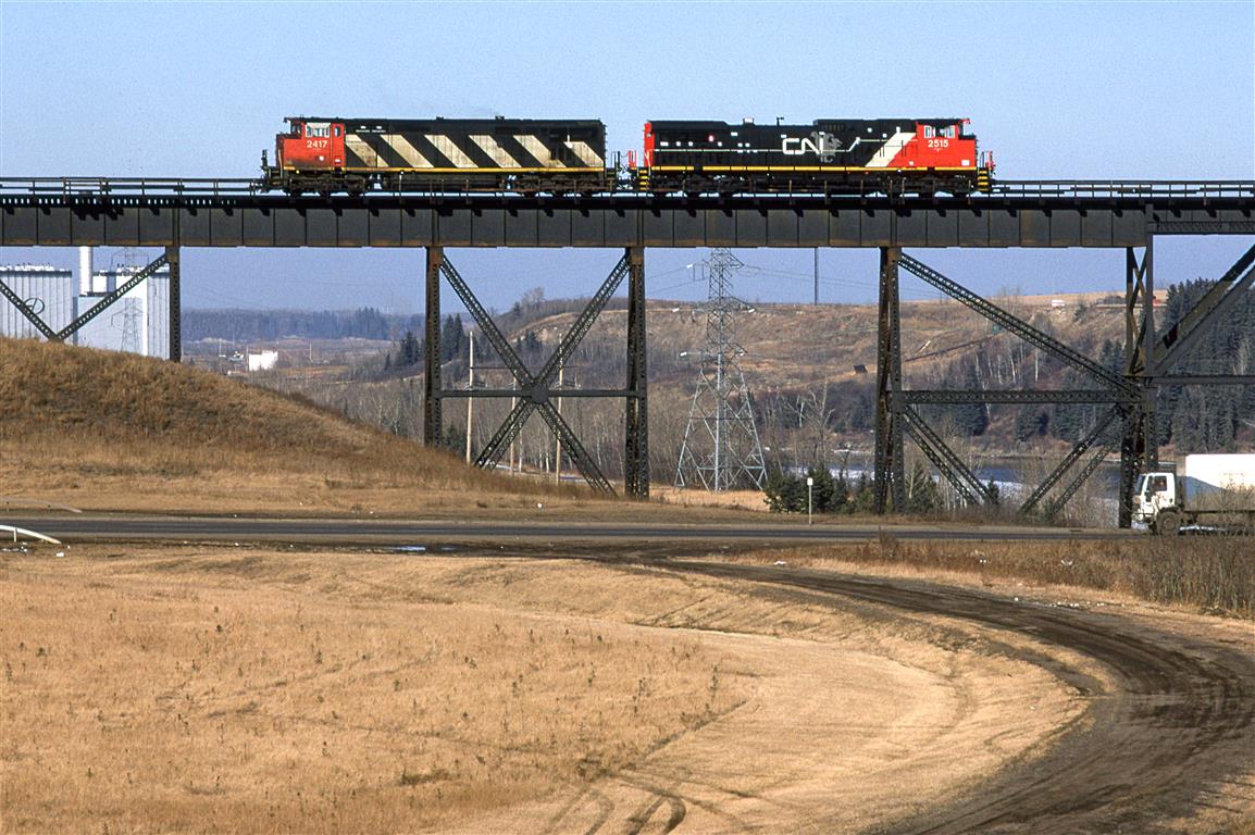 In an effort to try out different compositions of the CN bridge over the North Saskatchewan River, I came up with this.
Pictured is rescue power leaving town to help a crippled train on the Camrose Sub (Edmonton toward Calgary). I lacked patience in the day to see what they had to retrieve.
This may not be my first shot of the standard GE's on CN, but it is one of the first. Personally, I think the cowled units looked more refined, and I have always liked the stripes.