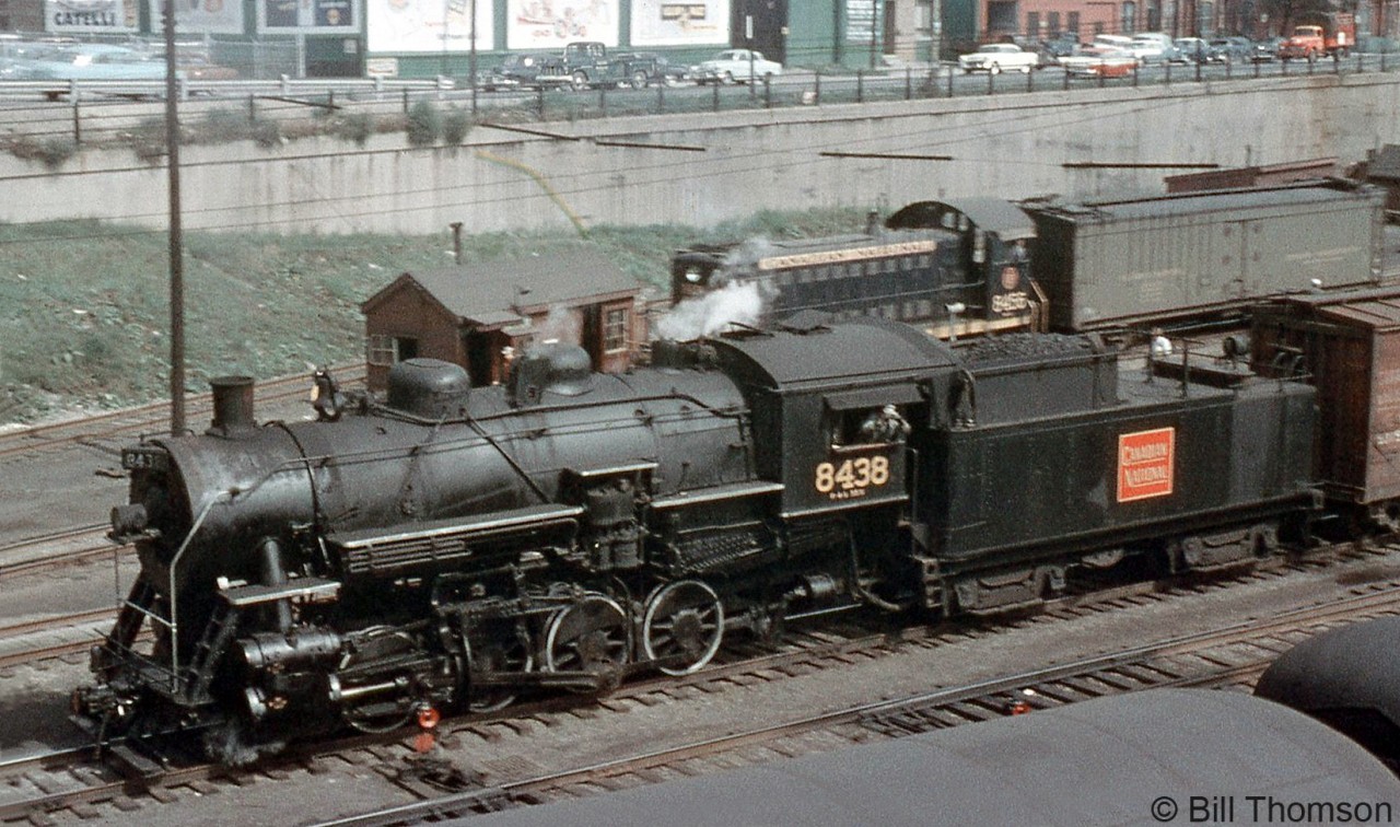 CN 0-8-0 switcher 8438 (a P4b-class unit built by the Grand Trunk in 1923) is seen switching cars at Bathust Street in busy downtown Toronto in 1958. In the late 1950's, diesels were slowly taking over the last of the steam assignments, as evident by MLW S3 8456 switching a passenger express reefer nearby. 8438 too would soon be replaced, and eventually scrapped in August 1961.