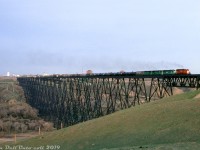 A light plume of exhaust drifts across the Oldman River as CP SD40-2 5614 leads BN B32-8 "B-Boats" 5499, 5498 and 5497 on a freight across the famed Lethbridge Viaduct, a very large steel trestle (apparently the largest in the world) that was originally built in 1907-1909 and continues to see freight service today, over 100 years since it was originally constricted.<br><br>The three "BN" B32-8's were actually pre-production GE Test bed/demo units built in 1984 that were just painted for Burlington Northern. They demonstrated on CP in 1985, but inevitably produced no orders for these high-horsepower 4-motor units (CP had just finished bulking up on 6-axle GMD SD40-2 units for mainline service, and was still taking delivery of scads of 4-motor GP38-2's for prairie branchline service at the time). After their demo stint they were leased by BN until being returned to owner GE in 1991. Research suggests unit 5497 was scrapped in the mid-90's, and 5498/99 lingered in a derelict state at GE in Erie PA until the early 2010's. In the end, the only roads to opt for the B32-8 model were Norfolk Southern and Amtrak.<br><br><i>Doug Wingfield photo, Dan Dell'Unto collection slide (with some colour correction/editing).</i>